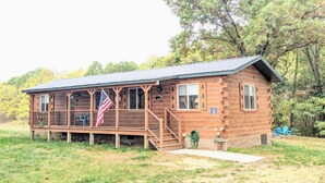 A wooden cabin with a porch, a flag, and a 'Welcome' sign.