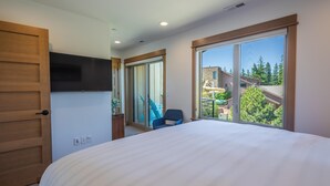 A bedroom with a large bed, a sliding door, a chair, and a view of a building and trees through a window.