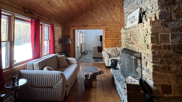A cozy cabin interior with wooden floors, a stone fireplace, a sofa, and a dining table. - Log Cabin Minutes from Jackson Gore and Okemo Mountain!!!!!!! (Wallingford)