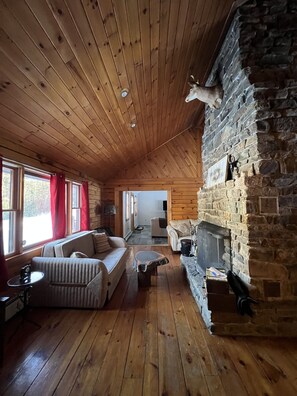 L’intérieur chaleureux d’un chalet avec un plancher en bois, une cheminée en pierre, un canapé et une table à manger.