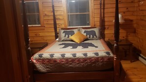 A wooden cabin room with a bed featuring a bear-themed bedspread and pillows, a nightstand, and a window with blinds. - Log Cabin Minutes from Jackson Gore and Okemo Mountain!!!!!!! (Wallingford)