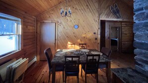A cozy cabin with a wooden interior, a dining table with chairs, a chandelier, and a stone wall. - Log Cabin Minutes from Jackson Gore and Okemo Mountain!!!!!!! (Wallingford)