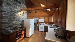 A rustic kitchen with a stone wall, wooden cabinets, a white refrigerator, a stove, and a microwave. - Log Cabin Minutes from Jackson Gore and Okemo Mountain!!!!!!! (Wallingford)