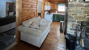 A cozy cabin interior with a wooden ceiling, a stone fireplace, a kitchen area, and a sofa with patterned cushions. - Log Cabin Minutes from Jackson Gore and Okemo Mountain!!!!!!! (Wallingford)