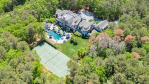 An aerial view of a large estate with a swimming pool, tennis court, and expansive wooded surroundings. - Chic Hamptons Retreat in Watermill with Tennis, Pool, Spa, Steam Room, and Gym (Water Mill)