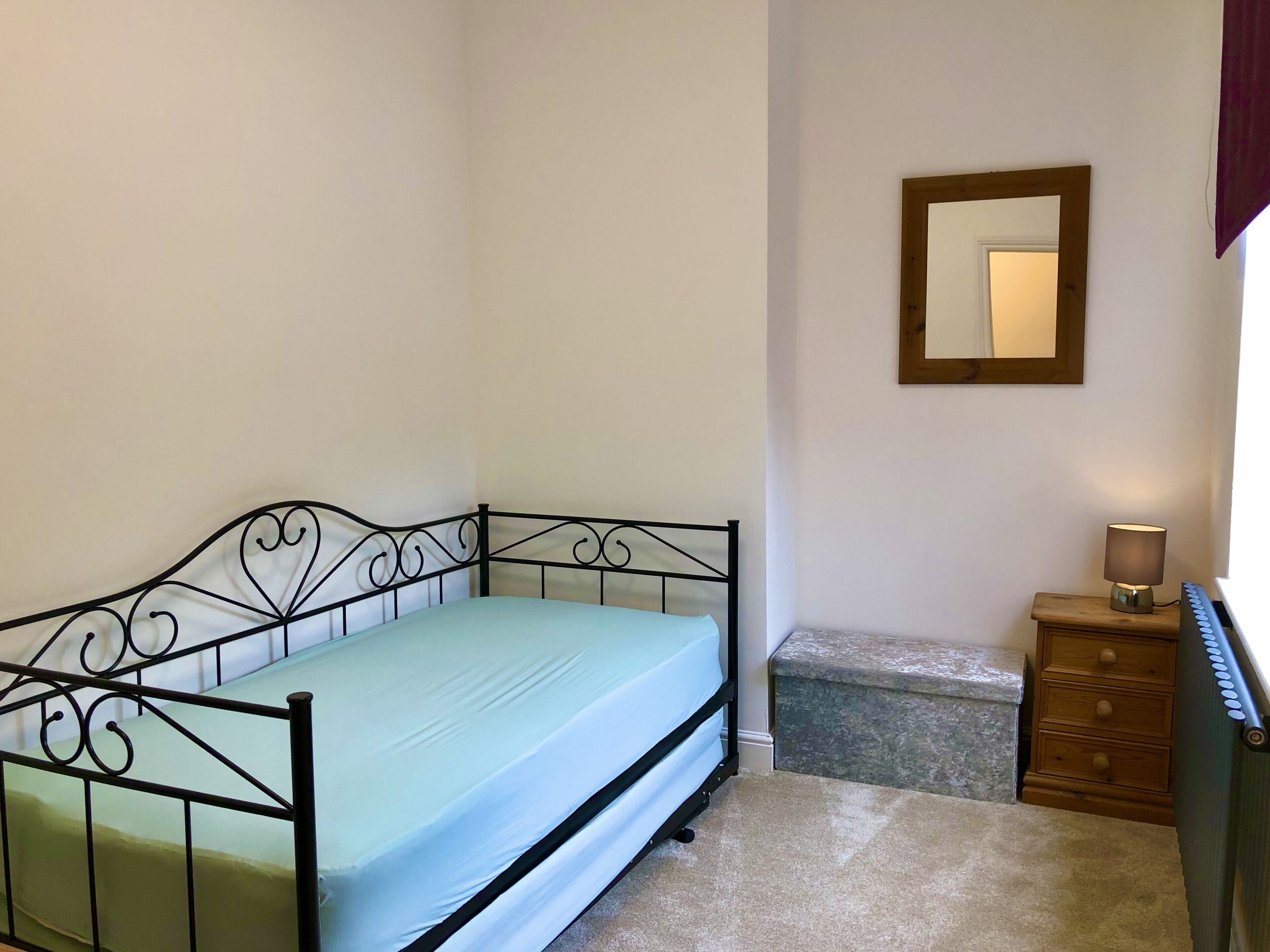 A single bed with a metal frame and a light blue mattress in a room with white walls.
