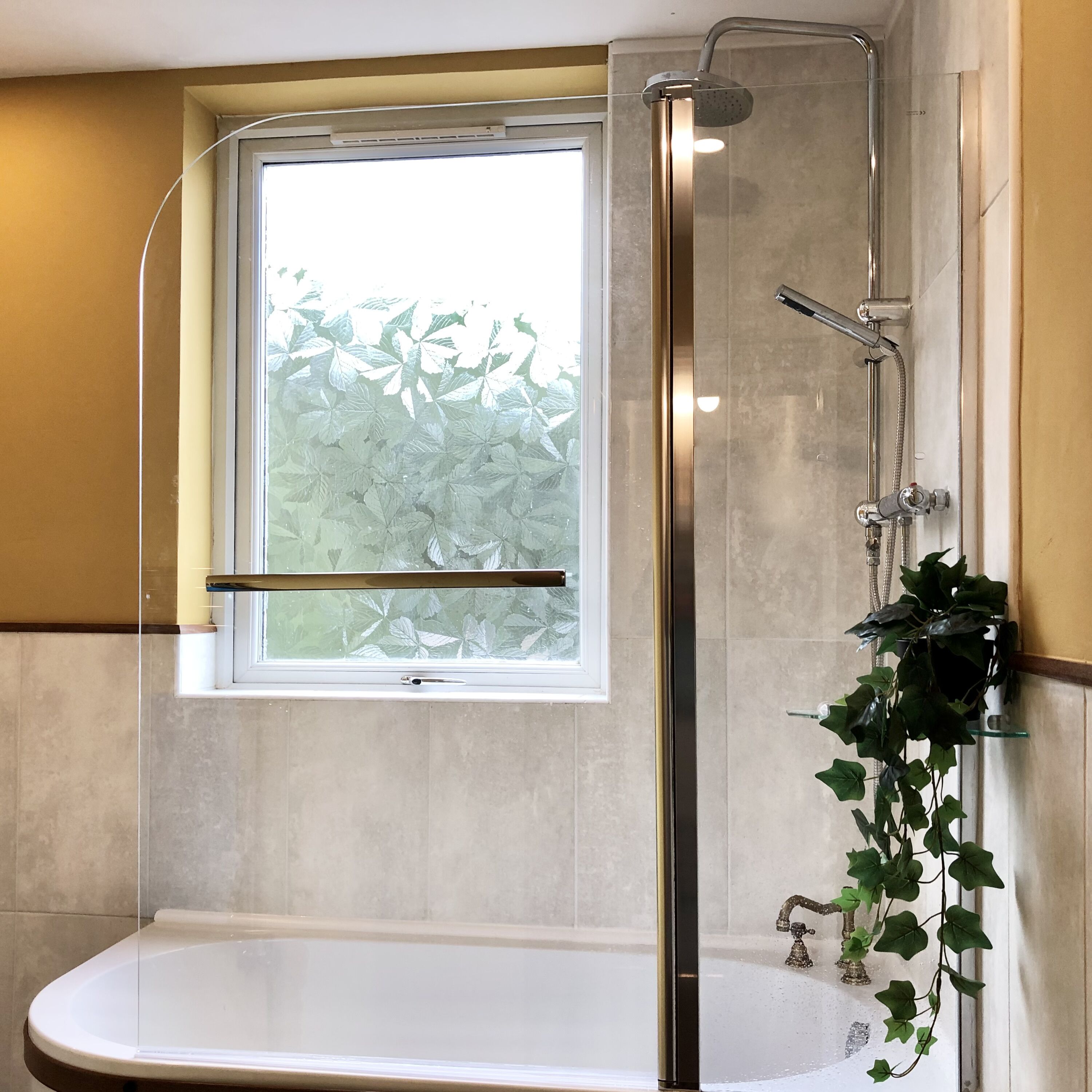 Un bagno moderno con doccia vetrata, una vasca e una finestra vista vegetazione.