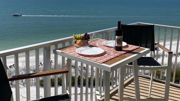 A deck with a table set for two, overlooking a beach and the ocean. - One Bedroom Direct Gulf Front View (FORT MYERS)