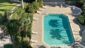 A rooftop pool with a tiled deck, surrounded by palm trees and lounge chairs. - One Bedroom Direct Gulf Front View (FORT MYERS)