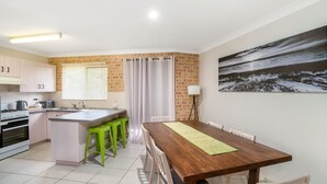 A compact kitchen with a central island, a dining area with a wooden table, and a large landscape painting on the wall.
