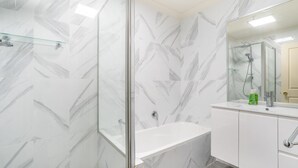 A modern bathroom with a glass shower enclosure, a white bathtub, and a vanity with a mirror.