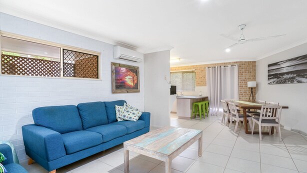 A modern living room with a blue sofa, a wooden coffee table, and a dining area with a wooden table and chairs.