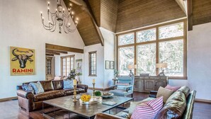 A spacious living room with leather sofas, a glass coffee table, and a chandelier.