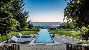 A swimming pool with a view of mountains, surrounded by greenery and deck chairs.