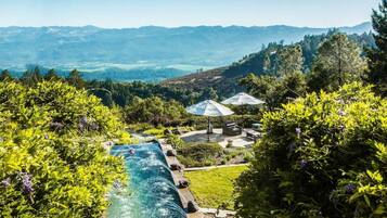 Una piscina con cascada, mobiliario exterior y vistas a colinas distantes.