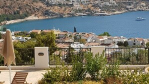 Un pueblo costero con vista al mar y a las montañas. Cuenta con un patio con una silla y plantas.