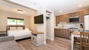 Una habitación pequeña con cama, un escritorio, televisor, kitchenette y zona de comedor.