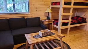 Interior acogedor de una cabaña con una cama litera de madera, un sofá, una mesita con una lámpara y vistas a través de una ventana.