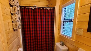 Baño de cabaña de madera con inodoro, lavamanos y cortina de ducha.