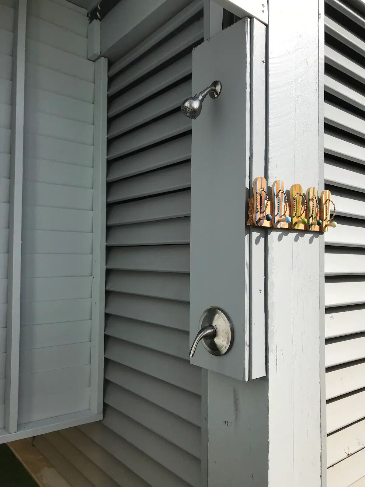 A white exterior wall with a metal door handle and a set of wooden flip-flops mounted on the wall.
