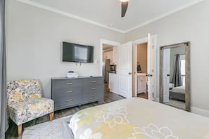 A bedroom with a bed, a grey dresser, a television on the wall, and a chair.