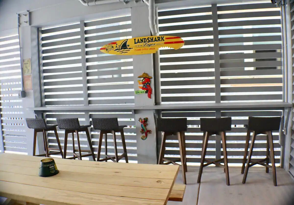A bar area with a wooden table and four chairs, a sign for 'Land Shark Island Style Lager', and a decorative wall piece.