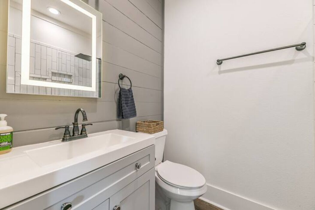 A bathroom with a white sink, a mirror, a towel ring, and a toilet.