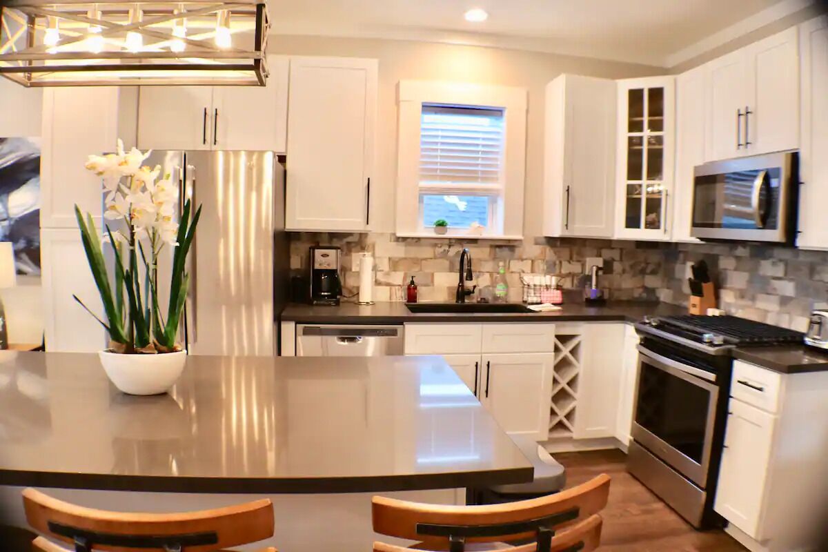 A modern kitchen with white cabinets, a central island with chairs, a built-in oven, and a microwave.