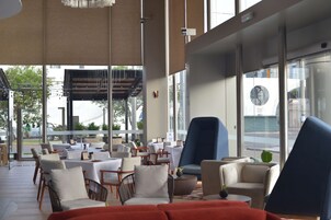 Un área de estar interior moderna con mesas y sillas, ventanas amplias y vistas al exterior.