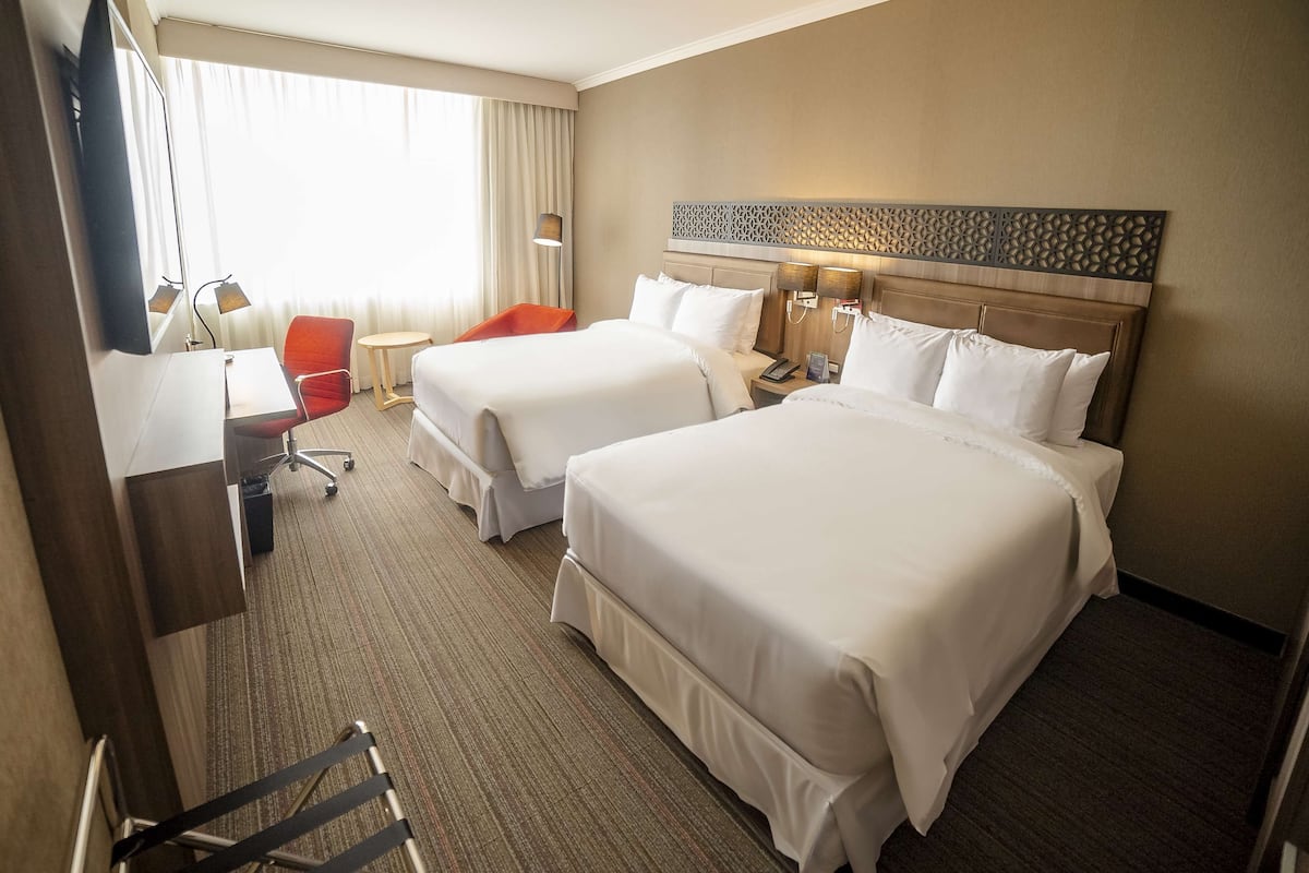 A hotel room with two beds, a desk, a chair, a TV, and a window with curtains.