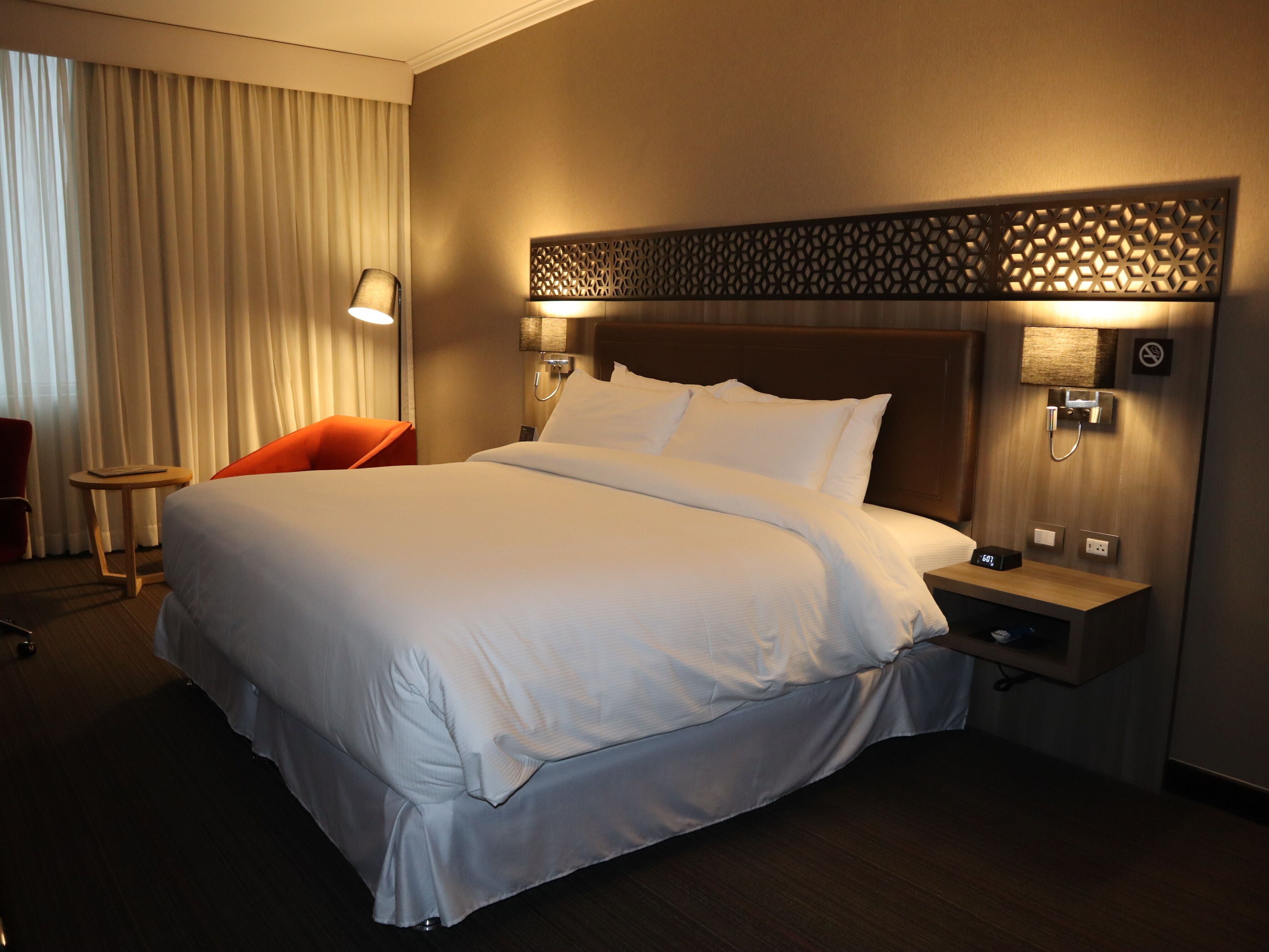 A hotel room with a large bed, two bedside tables, a nightstand, a chair, and a lamp.