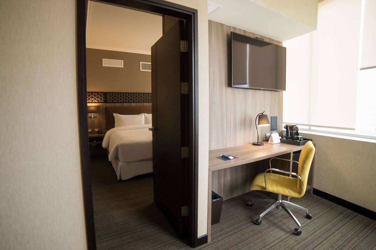A hotel room with a bed, a desk, a chair, a TV, and a window.