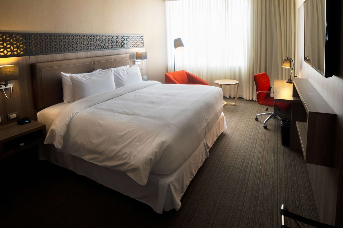 A hotel room with a large bed, a desk with a chair, a TV, and a window with curtains.