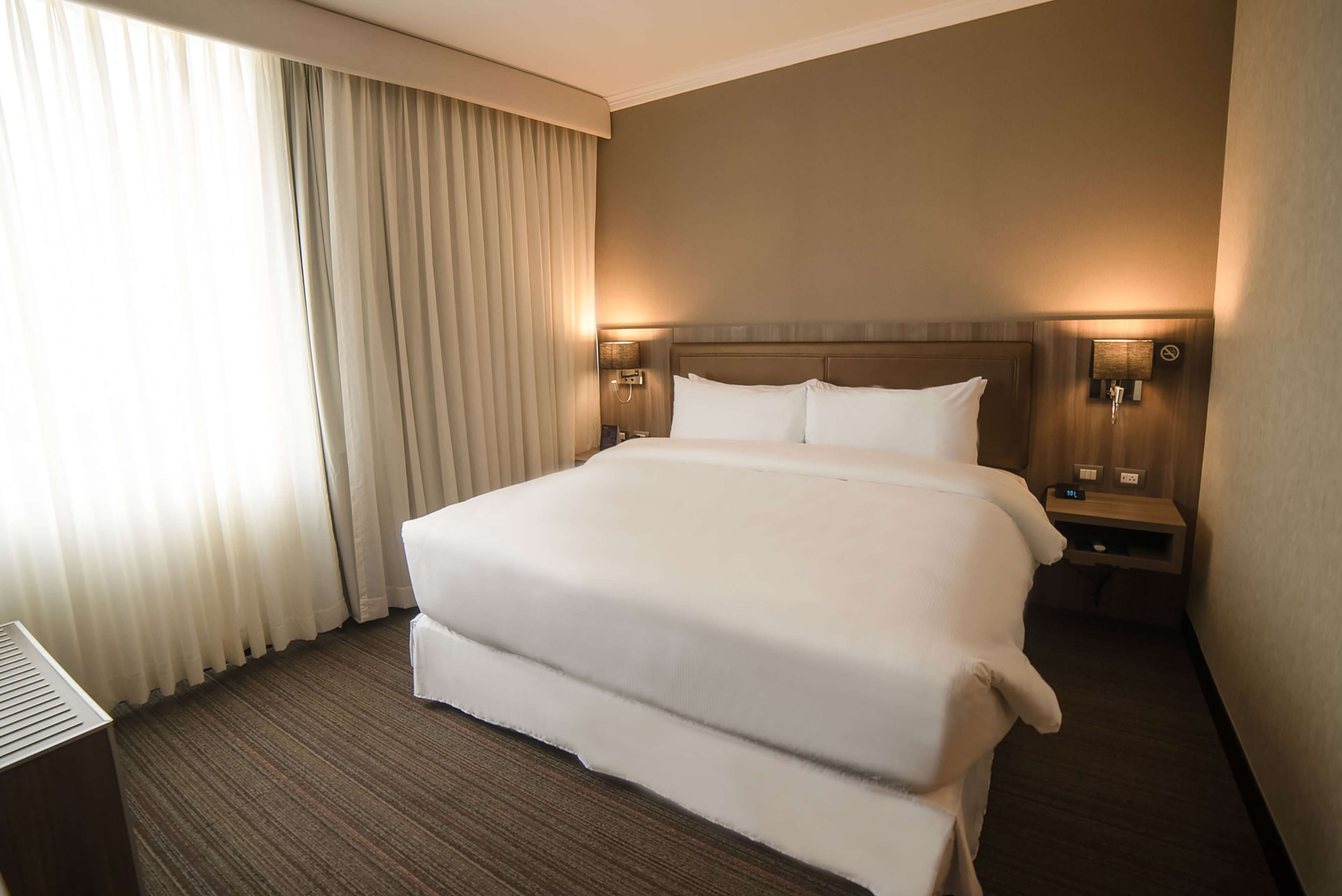 A hotel room with a large bed, two bedside tables, a nightstand, and a lamp.