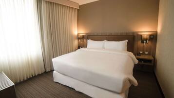 A hotel room with a large bed, two bedside tables, a nightstand, and a lamp.