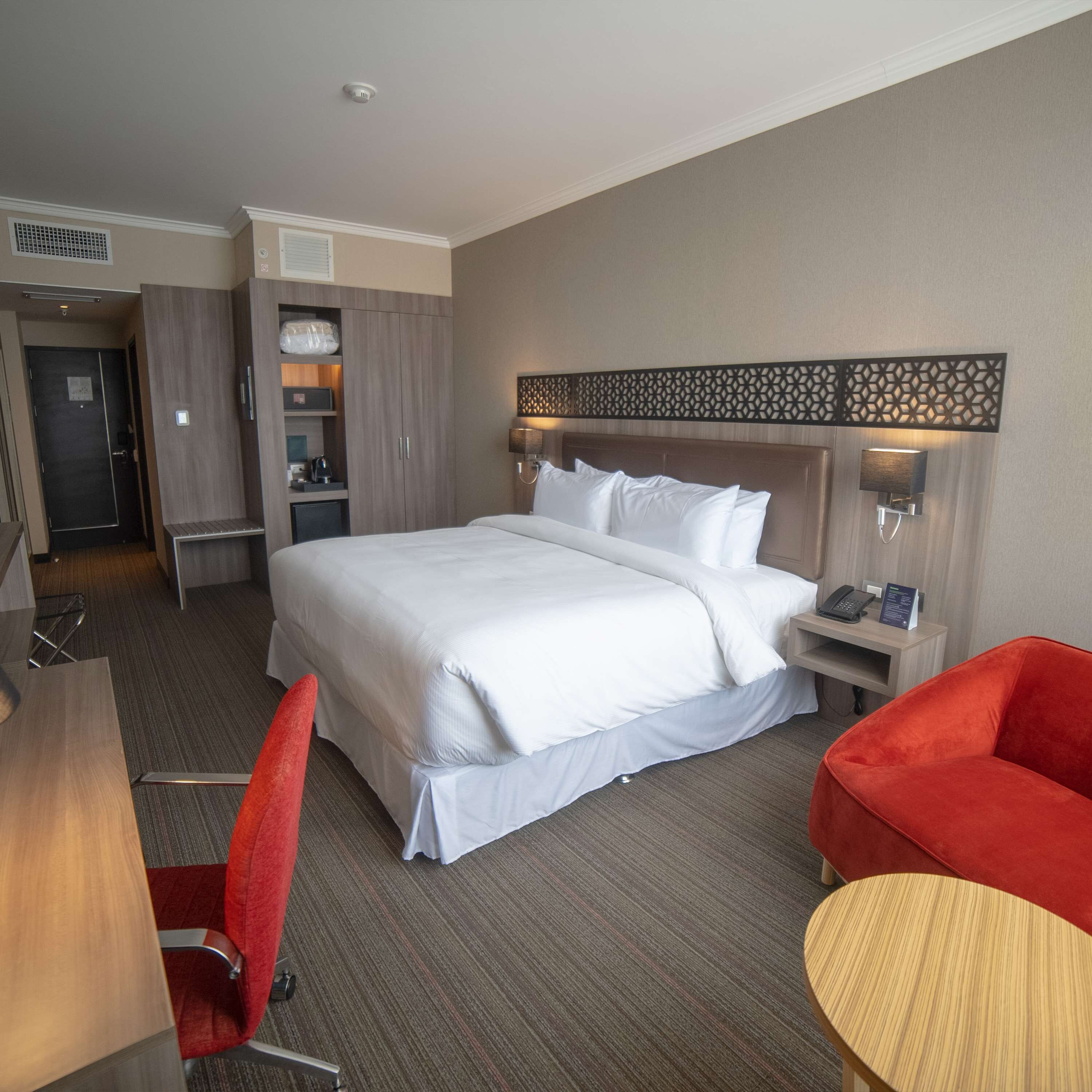 A hotel room with a large bed, a desk, a chair, and a small table.