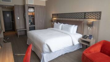 A hotel room with a large bed, a desk, a chair, and a small table.