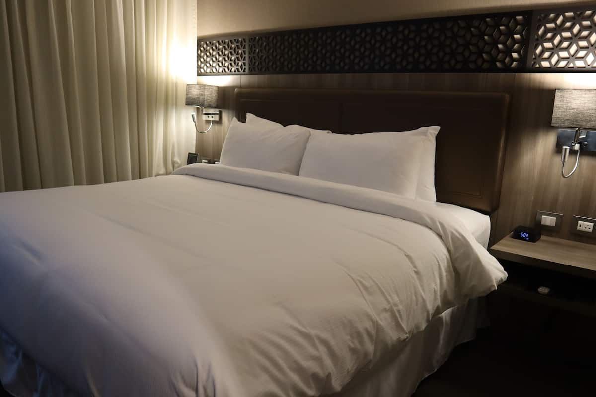 A hotel room with a large bed, a wooden headboard, and a nightstand with a digital clock.
