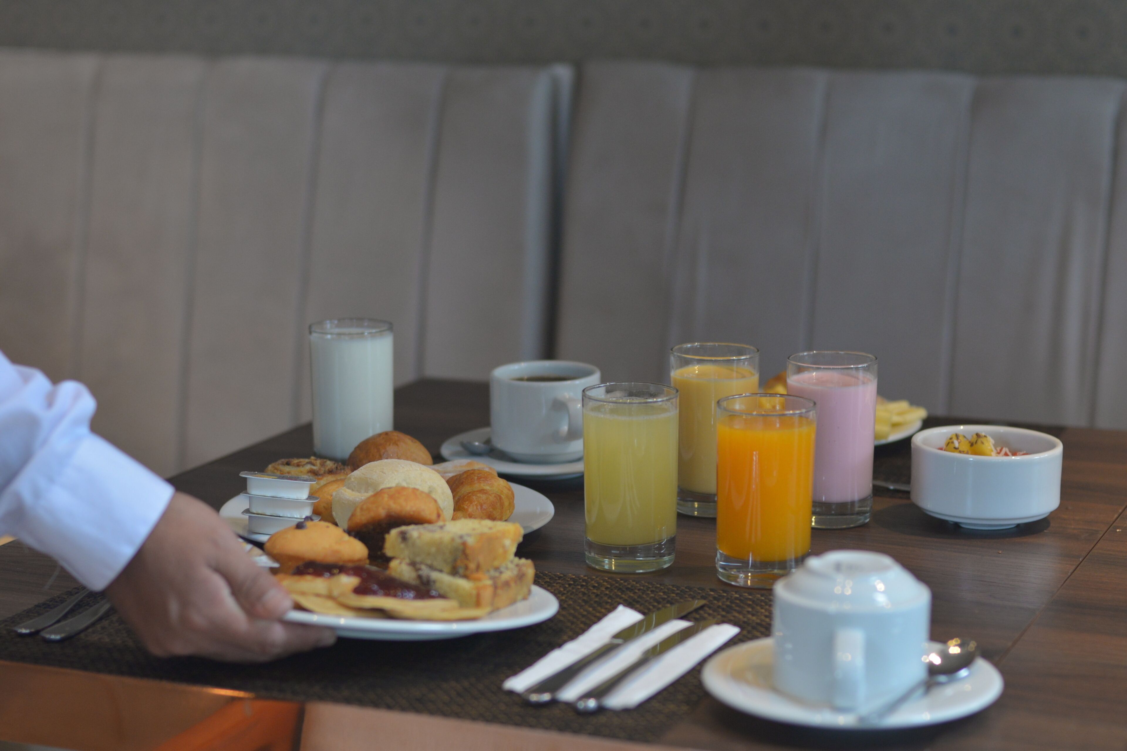 A breakfast table with plates of pastries, cups, and glasses of juice.
