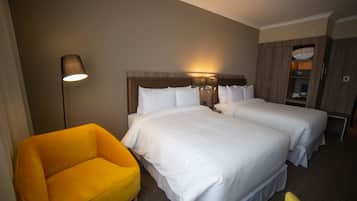 A hotel room with two beds, a nightstand, a lamp, and a yellow armchair.