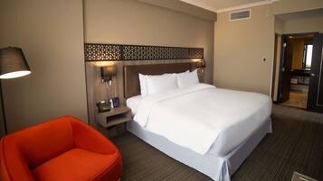 A hotel room with a large bed, a nightstand with a lamp and phone, a red chair, and a small table.