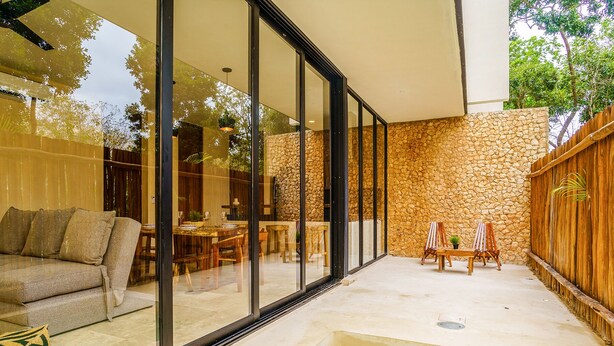 Un patio moderno al aire libre con pared de piedra, cerramiento de madera y zona de comedor con paredes de vidrio.