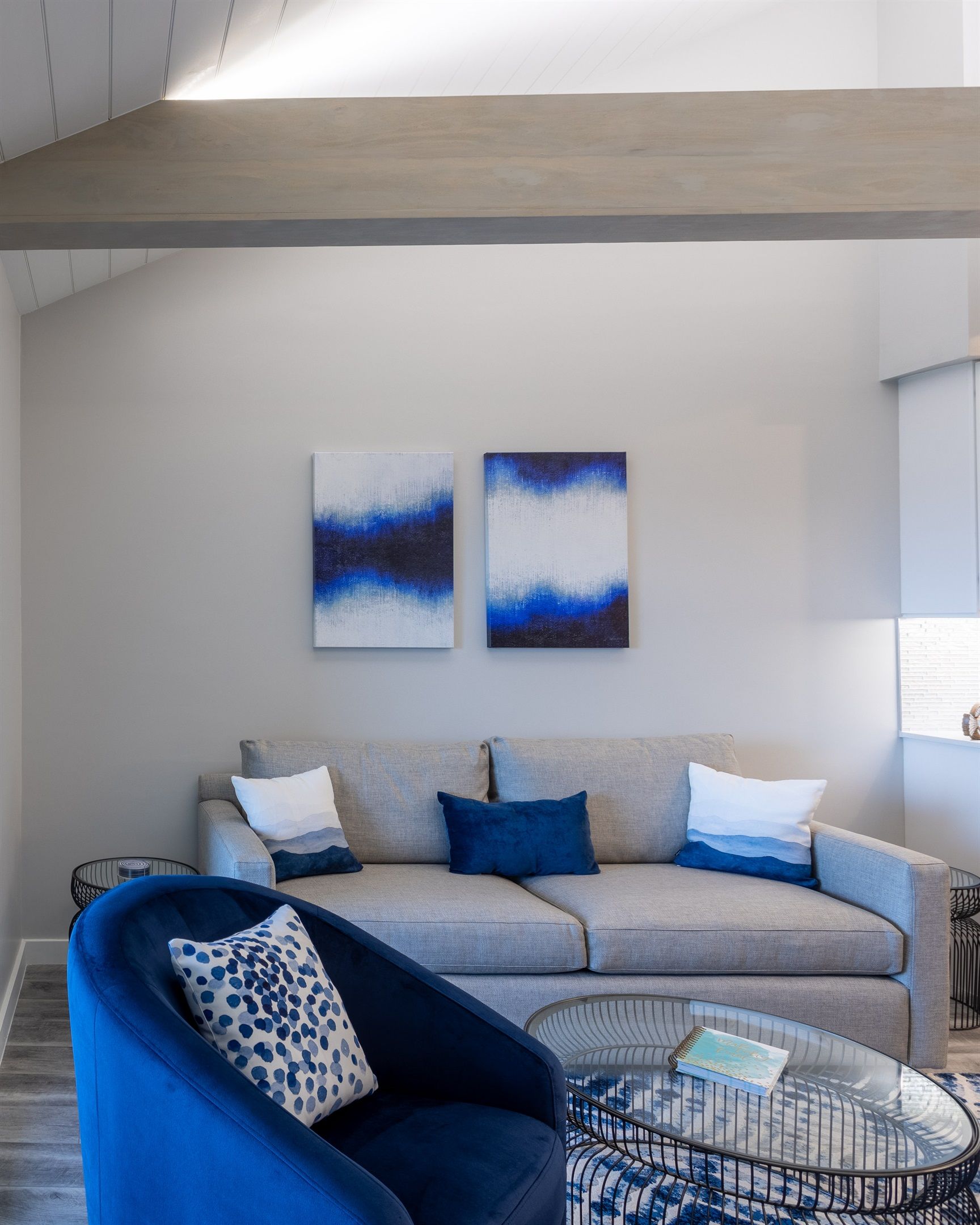 A modern living room with a grey sofa, blue armchair, and abstract art on the wall.