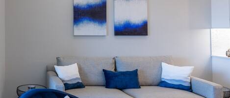 A modern living room with a grey sofa, blue armchair, and abstract art on the wall.