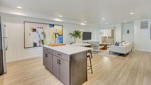 Eine moderne Küche mit Kochinsel, ein Essbereich mit rundem Tisch und ein Wohnzimmer mit Sofa und Fernseher.