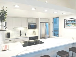 A modern kitchen with white cabinets, a stainless steel refrigerator, a microwave, and a large island with stools. - Walk to the Lifts! Park City 3BR Condo w/ Garage (Park City)