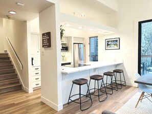 A modern kitchen with white cabinets, stainless steel appliances, and a bar area with stools. - Walk to the Lifts! Park City 3BR Condo w/ Garage (Park City)