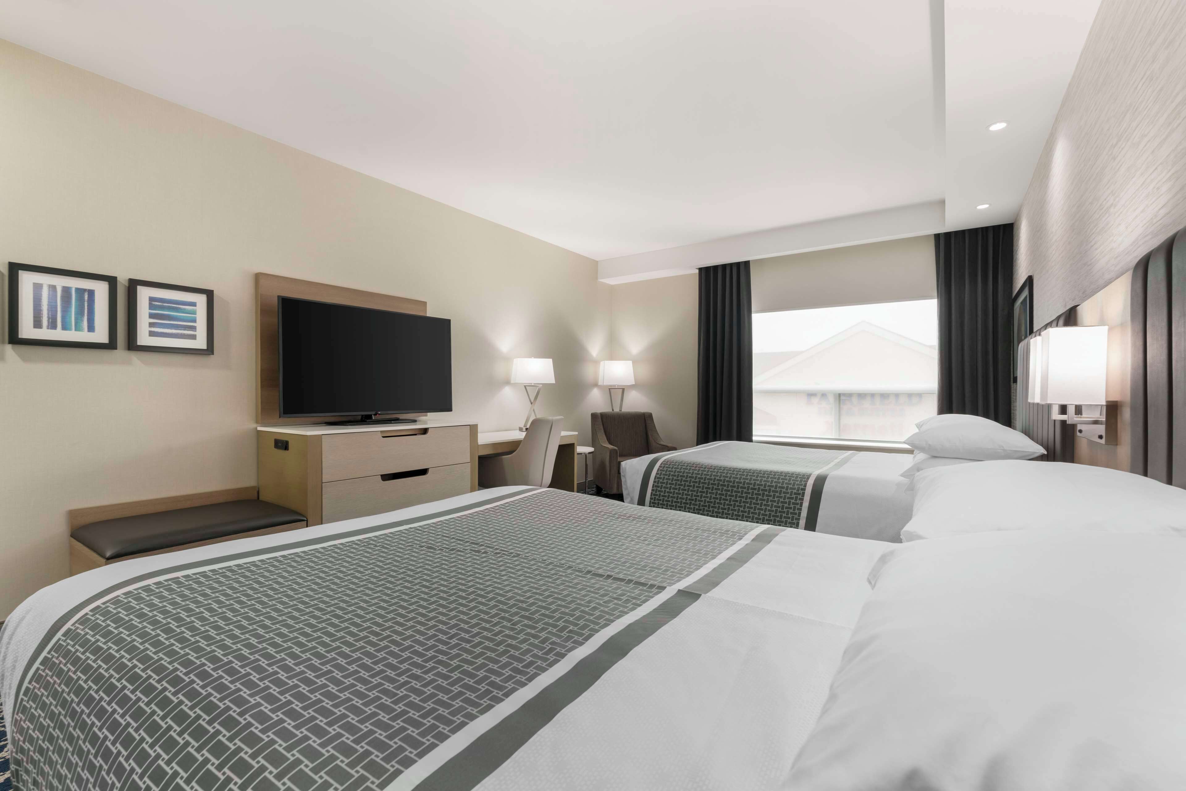 A hotel room with two beds, a desk, a television, and a window with curtains.