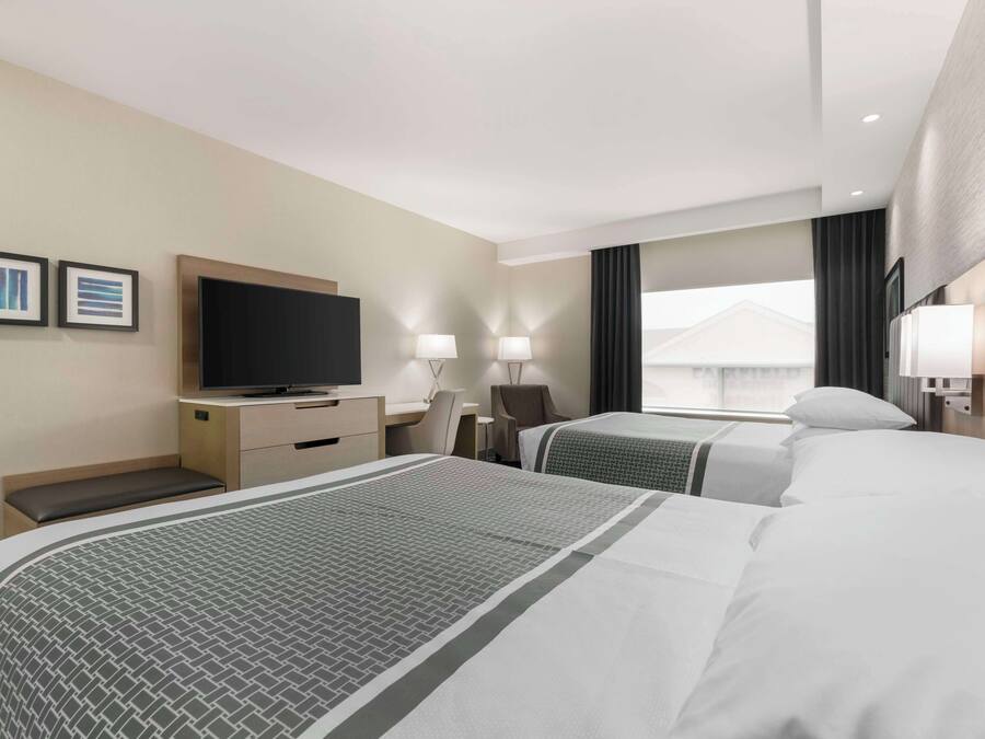 A hotel room with two beds, a desk, a television, and a window with curtains.