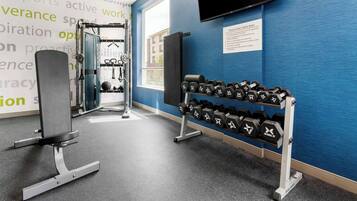 A gym with weightlifting equipment, dumbbells, and a TV mounted on the wall.